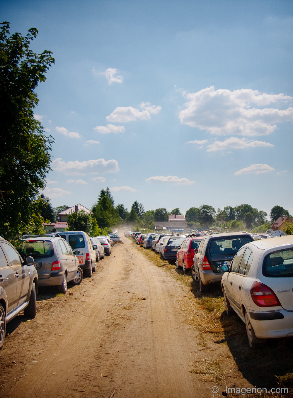 Two lines of cars parked by the dusty country road